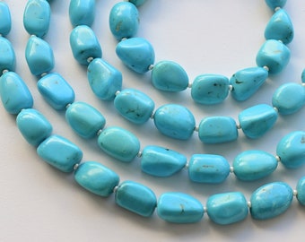 May include: A strand of turquoise beads, featuring a light blue colour and a smooth, rounded shape. The beads are strung on a silver cord and are arranged in a cascading pattern.