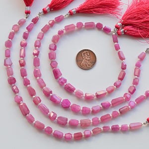 May include: Four strands of pink gemstone beads with faceted rectangular shapes. The beads are strung on silver wire and have tassels on the ends.