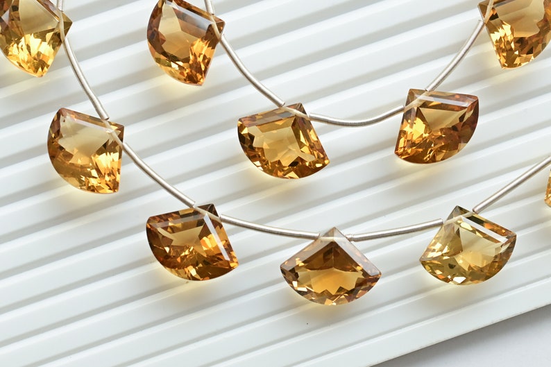 May include: A strand of golden citrine gemstone beads, each bead is a half-moon shape with a faceted cut. The beads are strung on a silver wire.