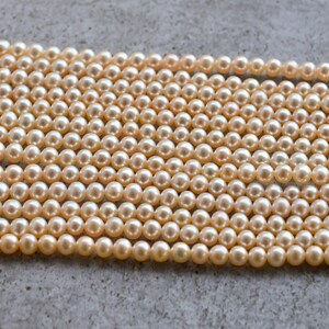May include: A strand of cream-colored pearls, arranged in rows on a gray surface. The pearls are round and smooth, with a subtle sheen.