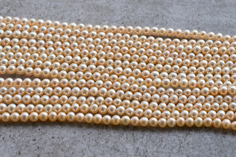 May include: A strand of cream-colored pearls, arranged in rows on a gray surface. The pearls are round and smooth, with a subtle sheen.