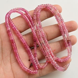 May include: A strand of pink tourmaline beads, each bead is square shaped and faceted. The beads are strung on a clear thread and are approximately 4mm in size.