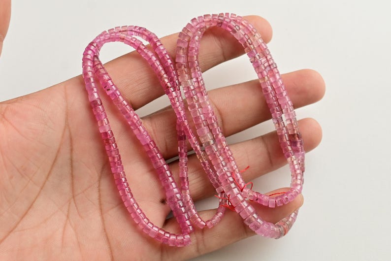 May include: A strand of pink tourmaline beads, each bead is square shaped and faceted. The beads are strung on a clear thread and are approximately 4mm in size.