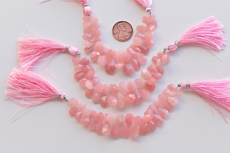 May include: Three strands of pink rose quartz gemstone beads with pink tassels. The beads are faceted and have a natural, irregular shape.