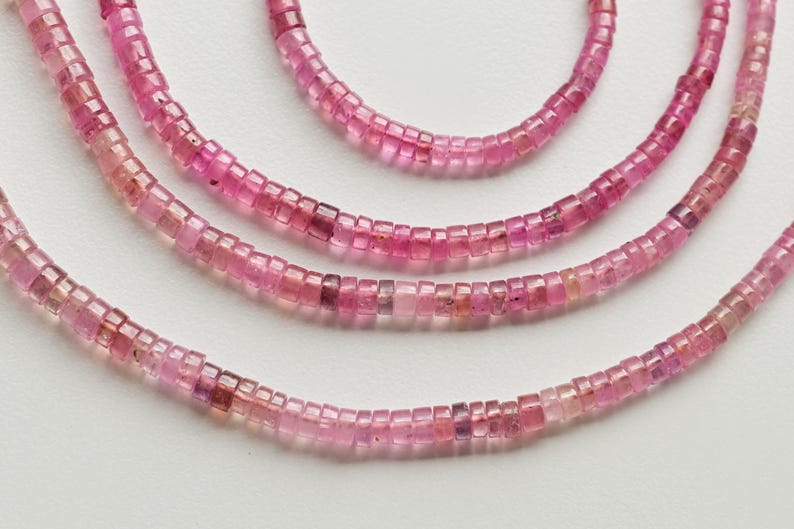 May include: Three strands of pink gemstone beads, each strand is made of small square-shaped beads.