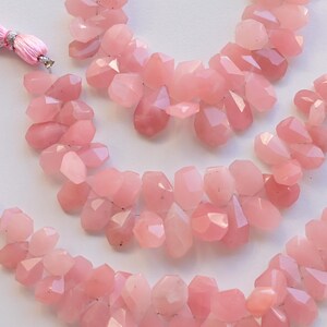 May include: Three strands of pink rose quartz gemstone beads, each strand is approximately 18 inches long and features faceted, teardrop-shaped beads. The beads are strung on a silver wire and have a tassel at each end.