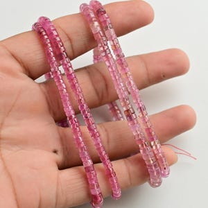 May include: Three strands of pink tourmaline beads, each strand is made of small, square-shaped beads. The beads are strung on a clear thread.