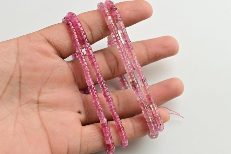May include: Three strands of pink tourmaline beads, each strand is made of small, square-shaped beads. The beads are strung on a clear thread.