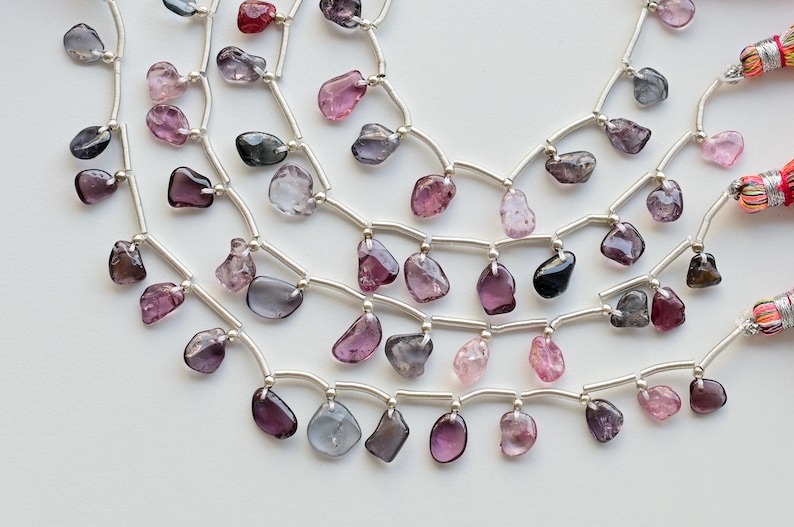 May include: A strand of silver chain with multiple rows of dangling, faceted, gemstone beads in shades of pink, purple, and gray.