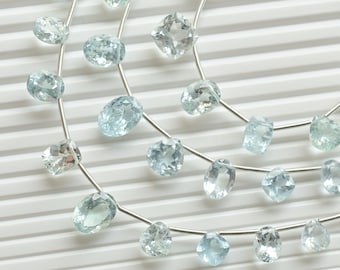 May include: A strand of light blue aquamarine gemstones strung on a silver wire. The gemstones are oval and pear shaped.