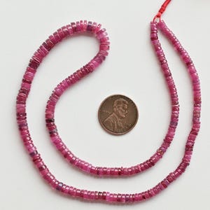 Puede incluir: Una hebra de cuentas de rubí rosa, de aproximadamente 40 cm de largo, con una moneda para la escala.