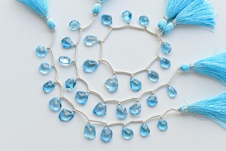May include: A strand of light blue gemstone beads with silver connectors and tassels. The beads are faceted and have a teardrop shape.