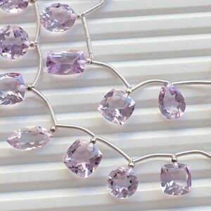 May include: A strand of pale lavender amethyst gemstone beads strung on a silver chain. The beads are faceted and have a variety of shapes, including square, oval, and pear.