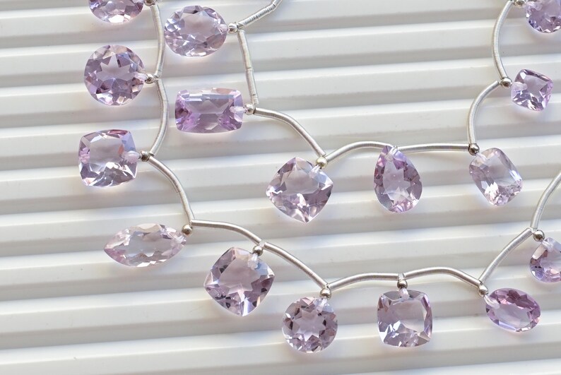 May include: A strand of pale lavender amethyst gemstone beads strung on a silver chain. The beads are faceted and have a variety of shapes, including square, oval, and pear.