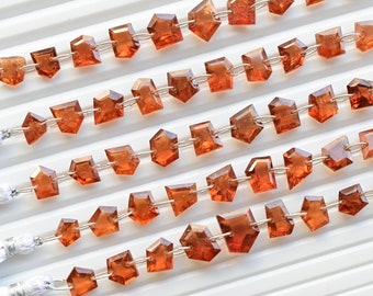 May include: A strand of orange gemstone beads, each bead is faceted and has a unique shape. The beads are strung on a silver wire and have a tassel at each end.