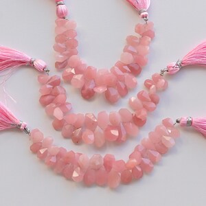 May include: Three strands of pink rose quartz gemstone beads with pink tassel accents. The beads are faceted and have a natural, irregular shape.