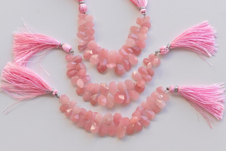 May include: Three strands of pink rose quartz gemstone beads with pink tassel accents. The beads are faceted and have a natural, irregular shape.