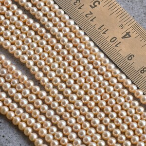 May include: A strand of cream-colored pearl beads, with a ruler in the background showing the beads are approximately 6mm in size.