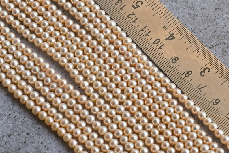 May include: A strand of cream-colored pearl beads, with a ruler in the background showing the beads are approximately 6mm in size.