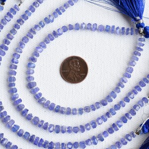 Może przedstawiać: Sznur jasnoniebieskich fasetowanych koralik&oacute;w z kamieni szlachetnych z srebrnym drutem przechodzącym przez środek. Koraliki są mniej więcej wielkości polskiej złot&oacute;wki. Sznur jest prezentowany z niebieskimi frędzlami.