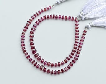 May include: Two strands of faceted, deep red gemstone beads. The beads are strung together with white string and silver-colored metal accents. White tassels are attached to the ends of the strands. The beads are a mix of shapes and sizes.