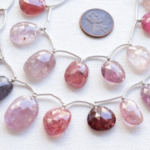 May include: A strand of faceted gemstone beads in shades of pink, purple, and blue. The beads are strung on silver wire and are approximately 1 cm in diameter.