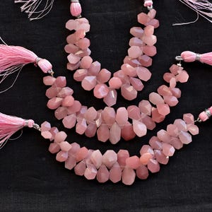May include: Three strands of pink gemstone beads with tassels on each end. The beads are faceted and have a light pink color.