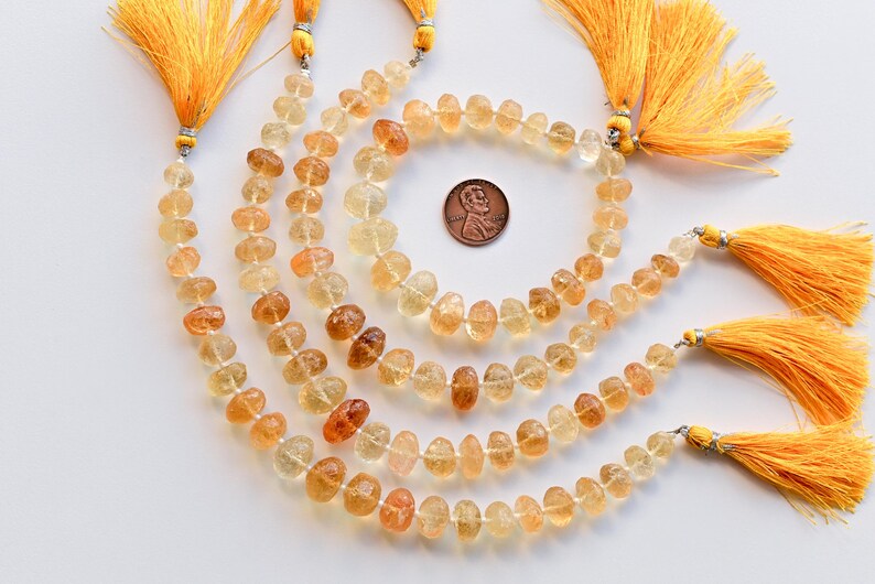May include: A strand of light yellow to amber colored gemstone beads. The beads are faceted and have a slightly irregular shape. The strand is approximately 18 inches long and is strung on a silver wire. The beads are separated by small silver spacers. The strand is finished with a silver clasp and a yellow tassel.