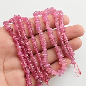 May include: A strand of pink tourmaline beads, with a faceted, elongated shape. The beads are strung on a thin thread and are ready for jewelry making.