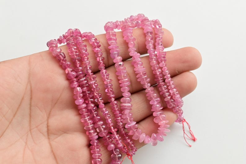 May include: A strand of pink tourmaline beads, with a faceted, elongated shape. The beads are strung on a thin thread and are ready for jewelry making.