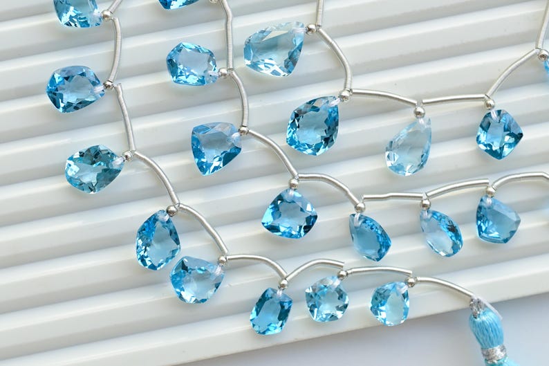 May include: A strand of light blue gemstone beads on a silver chain. The beads are faceted and have a teardrop shape. The chain is made of small silver beads.