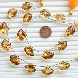 May include: A strand of 18 faceted, golden citrine gemstone beads, each shaped like a half-moon, strung on a silver wire. The beads are approximately the size of a US penny.