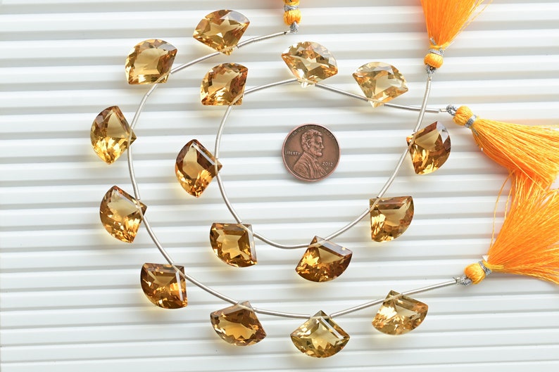 May include: A strand of 18 faceted, golden citrine gemstone beads, each shaped like a half-moon, strung on a silver wire. The beads are approximately the size of a US penny.