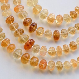 May include: A strand of light brown and orange gemstone beads. The beads are faceted and have a natural, irregular shape. The beads are strung on a clear thread.