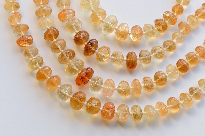May include: A strand of light brown and orange gemstone beads. The beads are faceted and have a natural, irregular shape. The beads are strung on a clear thread.
