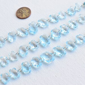 May include: A strand of light blue faceted crystal beads in a flower shape, strung on silver wire. The beads are approximately the size of a US quarter.