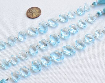 May include: A strand of light blue faceted crystal beads in a flower shape, strung on silver wire. The beads are approximately the size of a US quarter.