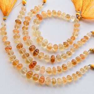 May include: A strand of golden citrine gemstone beads with a faceted, teardrop shape. The beads are strung on a cord with a tassel at each end. The tassels are a bright yellow color.