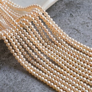 May include: A strand of cream-colored pearl beads, arranged in rows, on a gray textured surface.