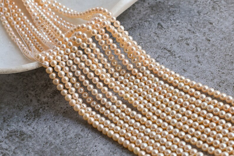 May include: A strand of cream-colored pearl beads, arranged in rows, on a gray textured surface.