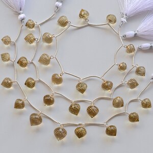 May include: A strand of brown gemstone beads with silver connectors and white tassels. The beads are heart-shaped and have a faceted finish.