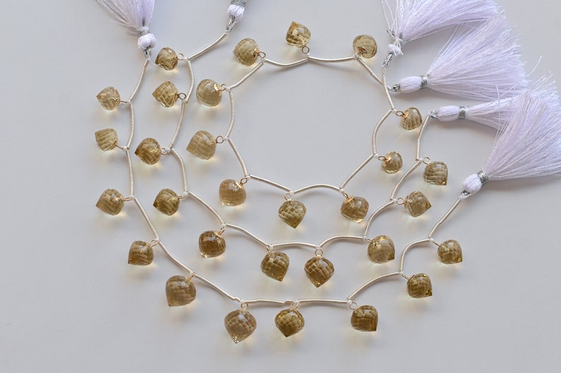 May include: A strand of brown gemstone beads with silver connectors and white tassels. The beads are heart-shaped and have a faceted finish.