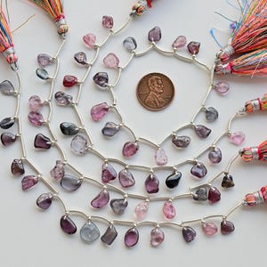 May include: A strand of faceted gemstone beads in shades of pink, purple, and blue, separated by silver spacers. The beads are strung on a silver chain and are approximately 10mm in size. The strand is accented with colorful tassels on each end.