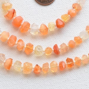 Puede incluir: Una hebra de cuentas de piedras preciosas de color naranja, amarillo y blanco. Las cuentas son facetadas y tienen una forma natural irregular.