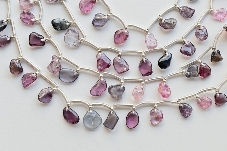 May include: A multi-strand necklace with silver chain and various shades of pink, purple, and gray gemstone beads.