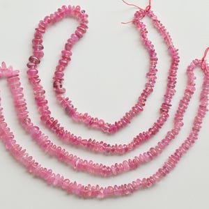 May include: Three strands of pink tourmaline gemstone beads. The beads are faceted and have a slightly irregular shape. The strands are of varying lengths.