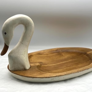 May include: A swan-shaped serving tray. The swan's head and neck are painted white with a brown beak. The oval tray is made of wood with a light brown finish and a white painted rim.