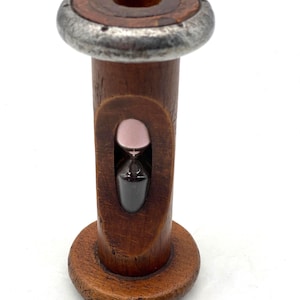 May include: A wooden hourglass with a dark brown finish. The hourglass has a metal rim around the top and a small hourglass visible in the center. The hourglass is a decorative item.