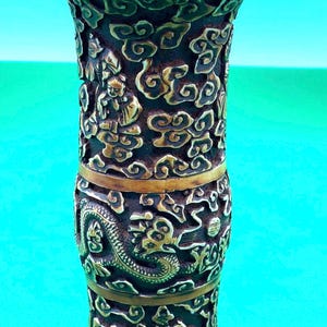 May include: A brown and gold ceramic vase with intricate carvings of clouds, dragons, and figures. The vase has a wide mouth and a narrow base.