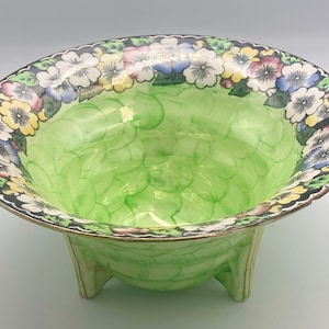 May include: A green ceramic bowl with a floral design around the rim. The bowl has three legs and a textured surface.